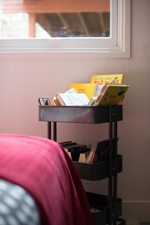 A shared bedroom for FOUR sisters. No room for a bookshelf, so a rolling library cart is used instead.