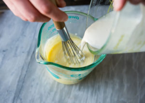 adding hot cream to egg yolks and sugar for creme brulee