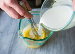 adding hot cream to egg yolks and sugar